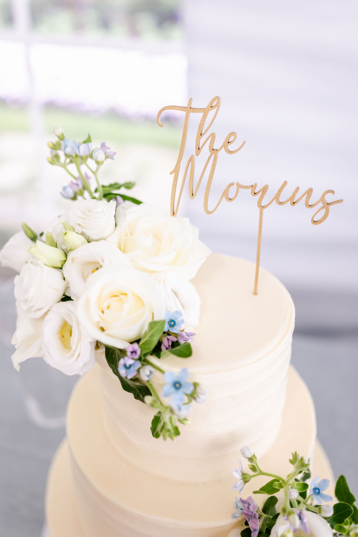 Elegant white wedding cake decorated with fresh flowers and gold script toppers.