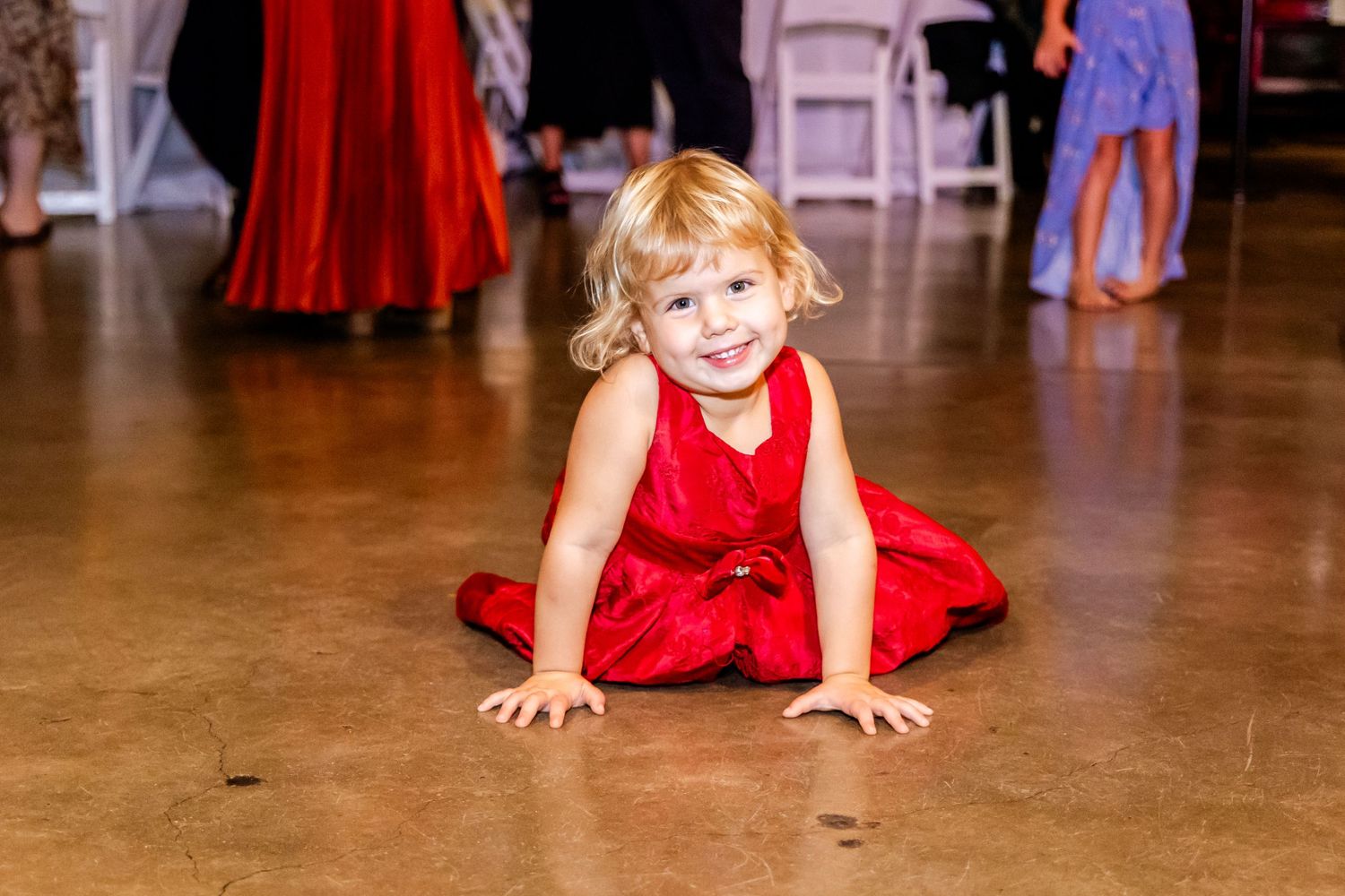 Young child in red dress plays on dance floor during wedding reception.