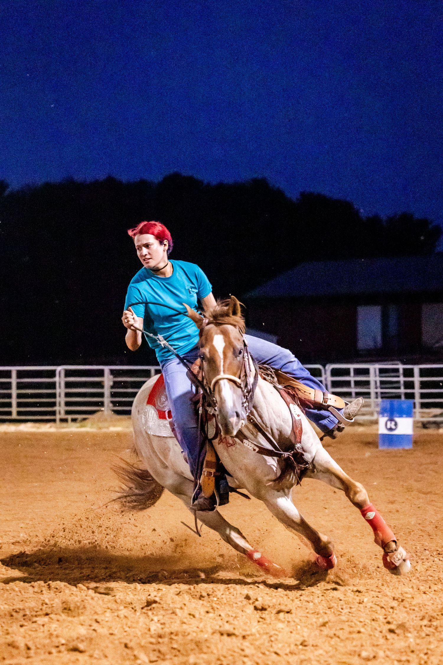 Dynamic sequence of a rider on horseback performing a barrel racing turn in an arena at night.