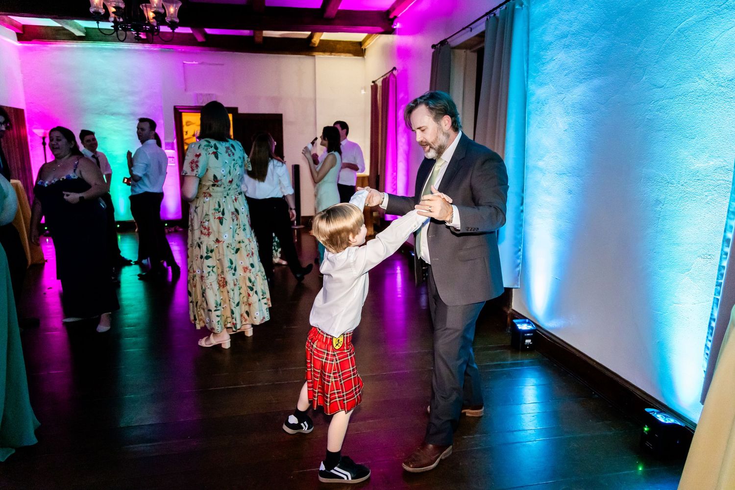 A suited adult dancing with a child in red dress at a wedding reception.