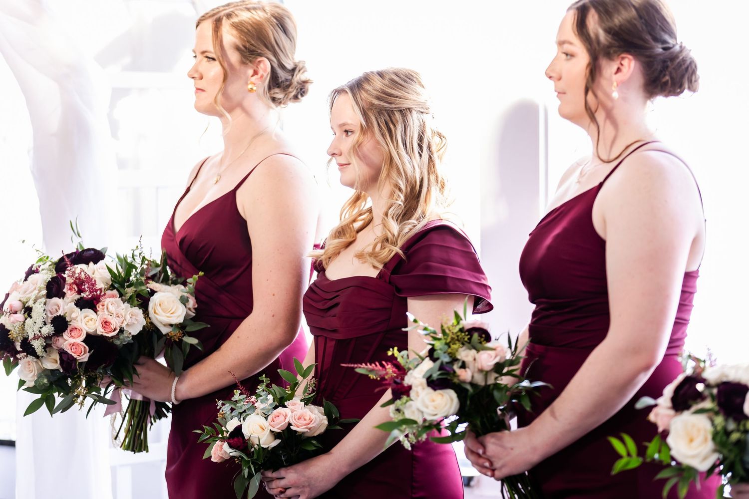 Bridesmaids in burgundy dresses hold white and pink floral bouquets.