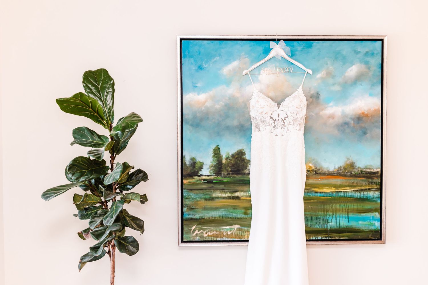 A layout of wedding dress, landscape artwork, and potted plants arranged against a light colored wall.