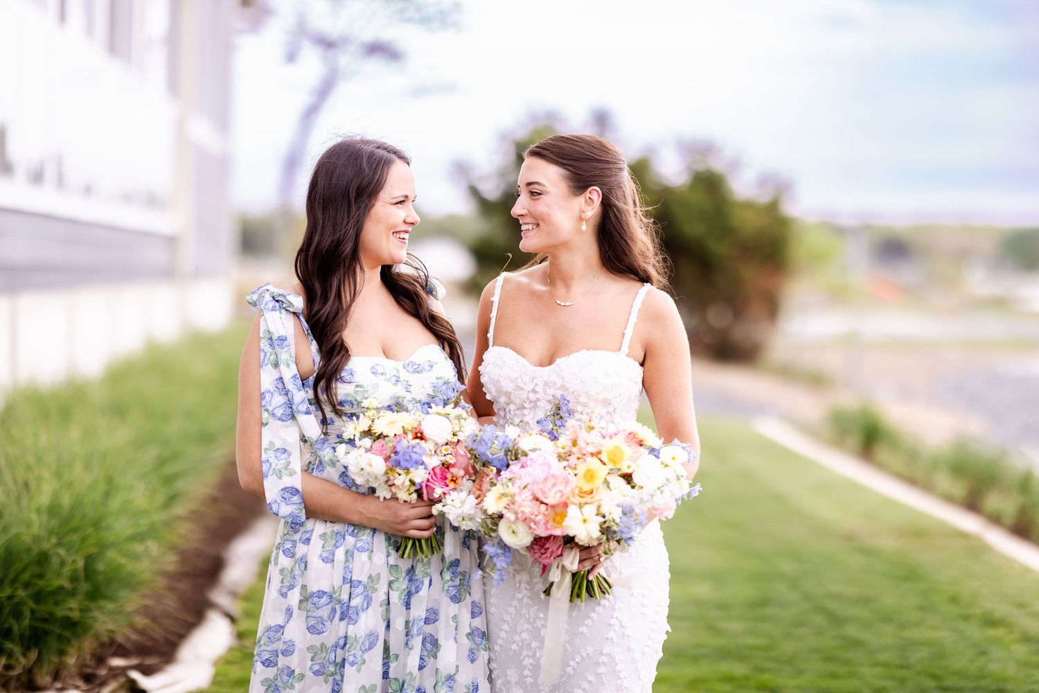 Bridesmaids in floral dresses share joyful moments outdoors on a sunny day.