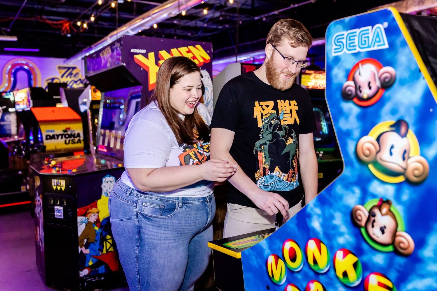 Two people enjoying a game of Monkey Ball at a retro arcade with classic SEGA games and neon lighting.