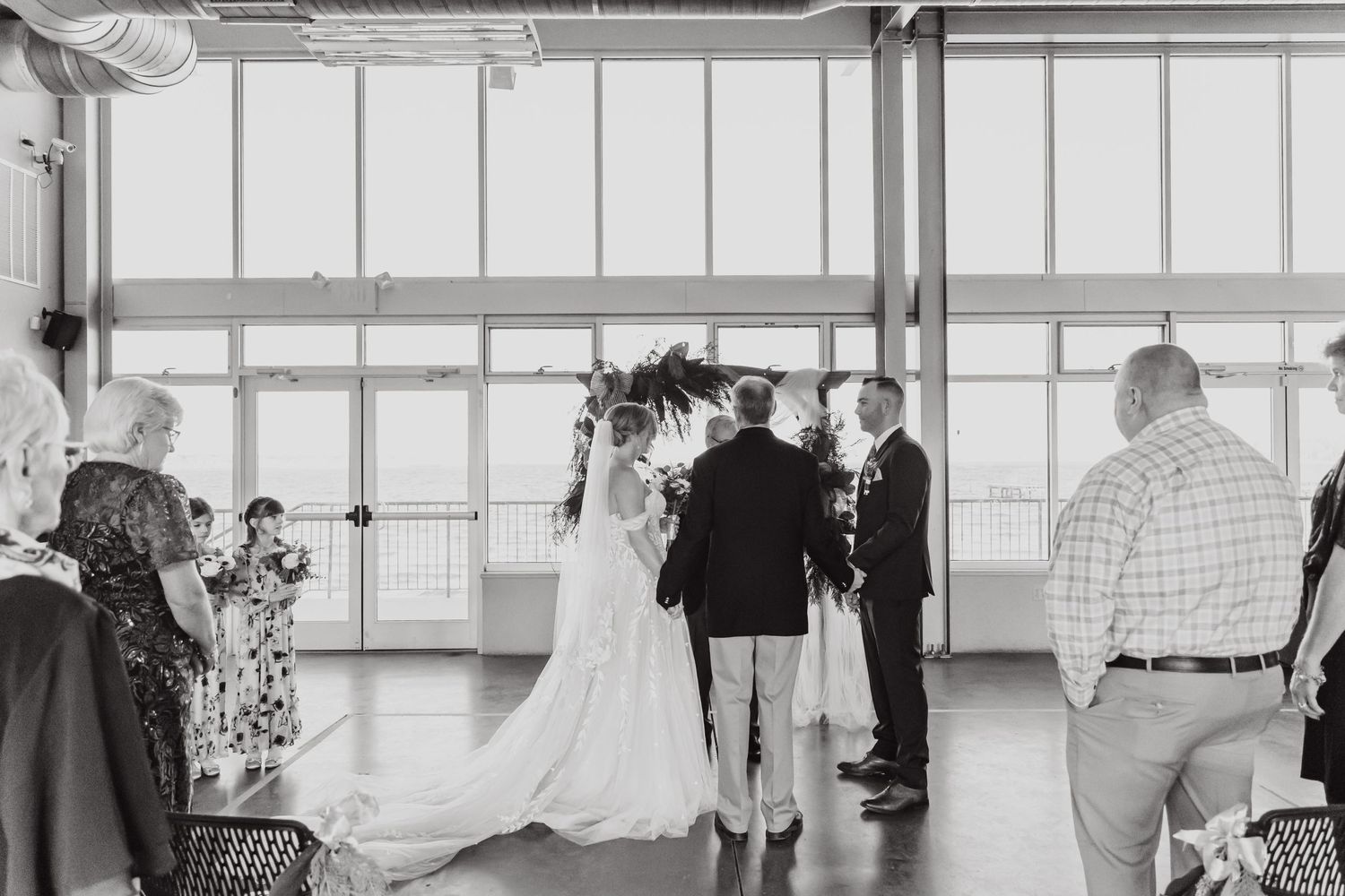 A wedding ceremony in progress inside a modern venue with large windows.