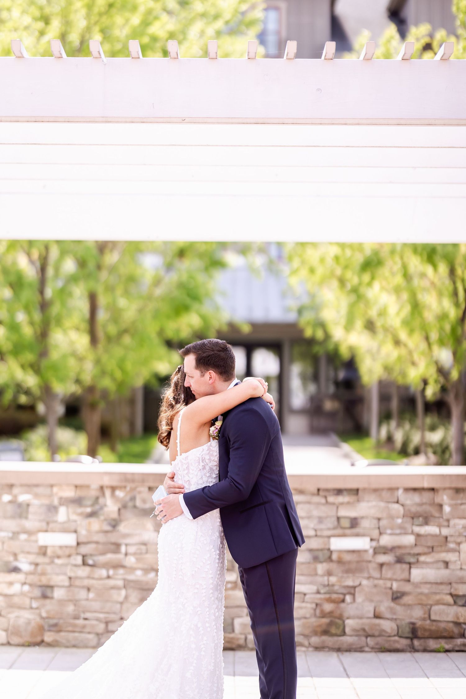 A romantic moment between newlyweds embracing in front of a stone wall during their outdoor wedding.