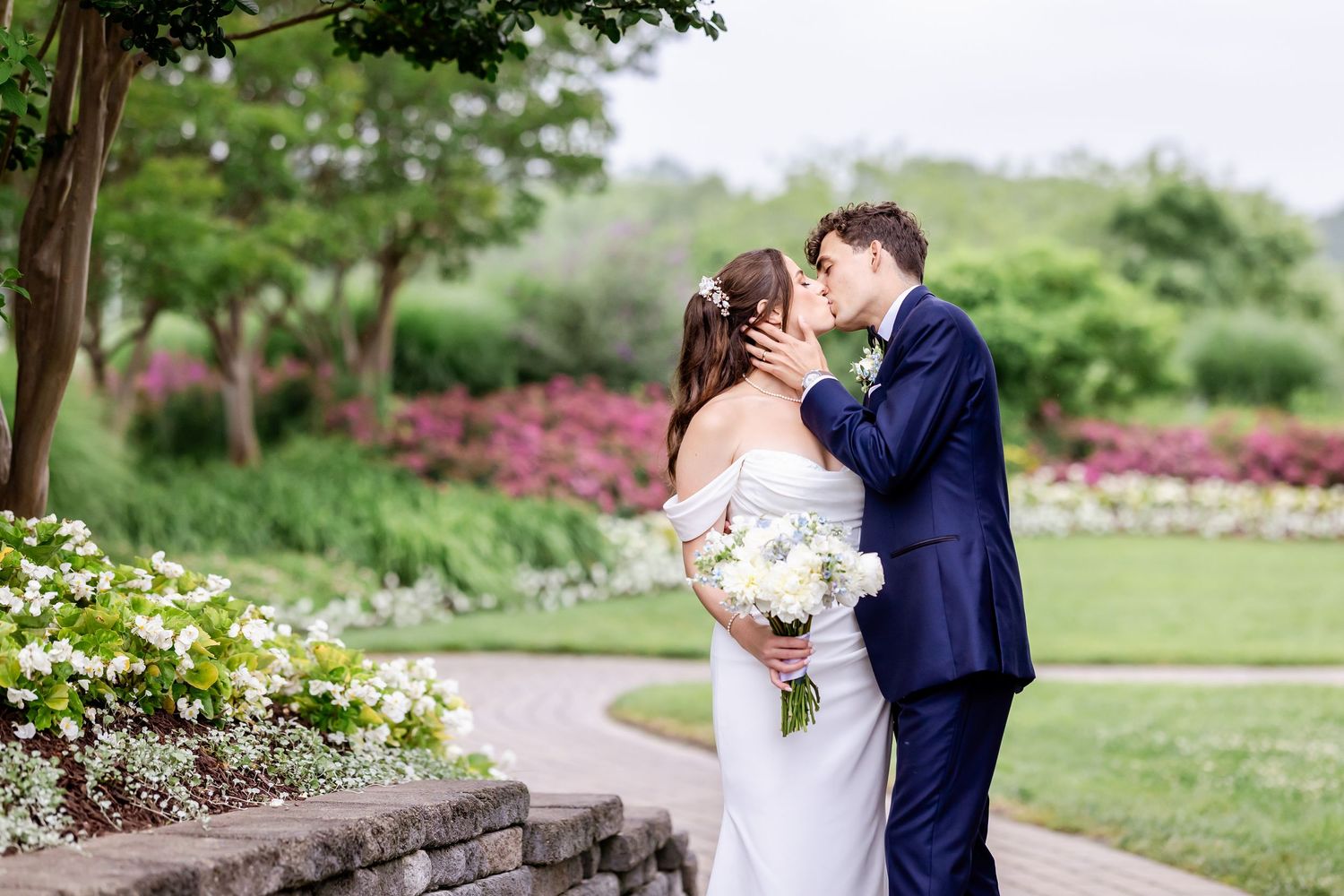 A couple in wedding attire embraces in a lush garden setting with blooming flowers and greenery.