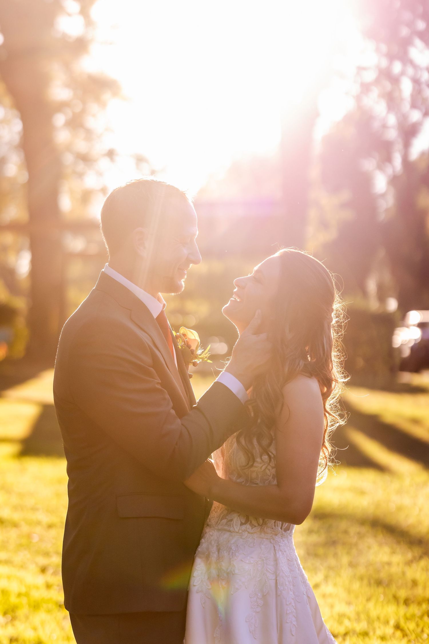Romantic sunset wedding portrait with golden sunlight streaming through trees in an outdoor setting.