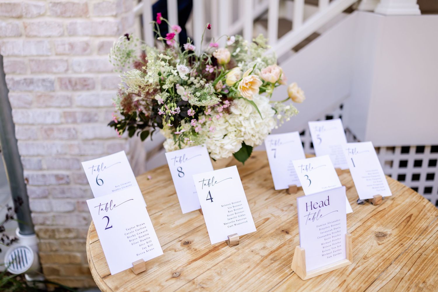 Wedding seating cards displayed on wooden table with fresh floral centerpiece arrangement.