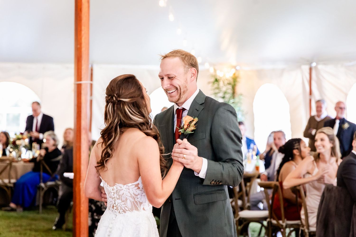 Couple shares their first dance together at an elegant wedding reception under a white tent with warm lighting.