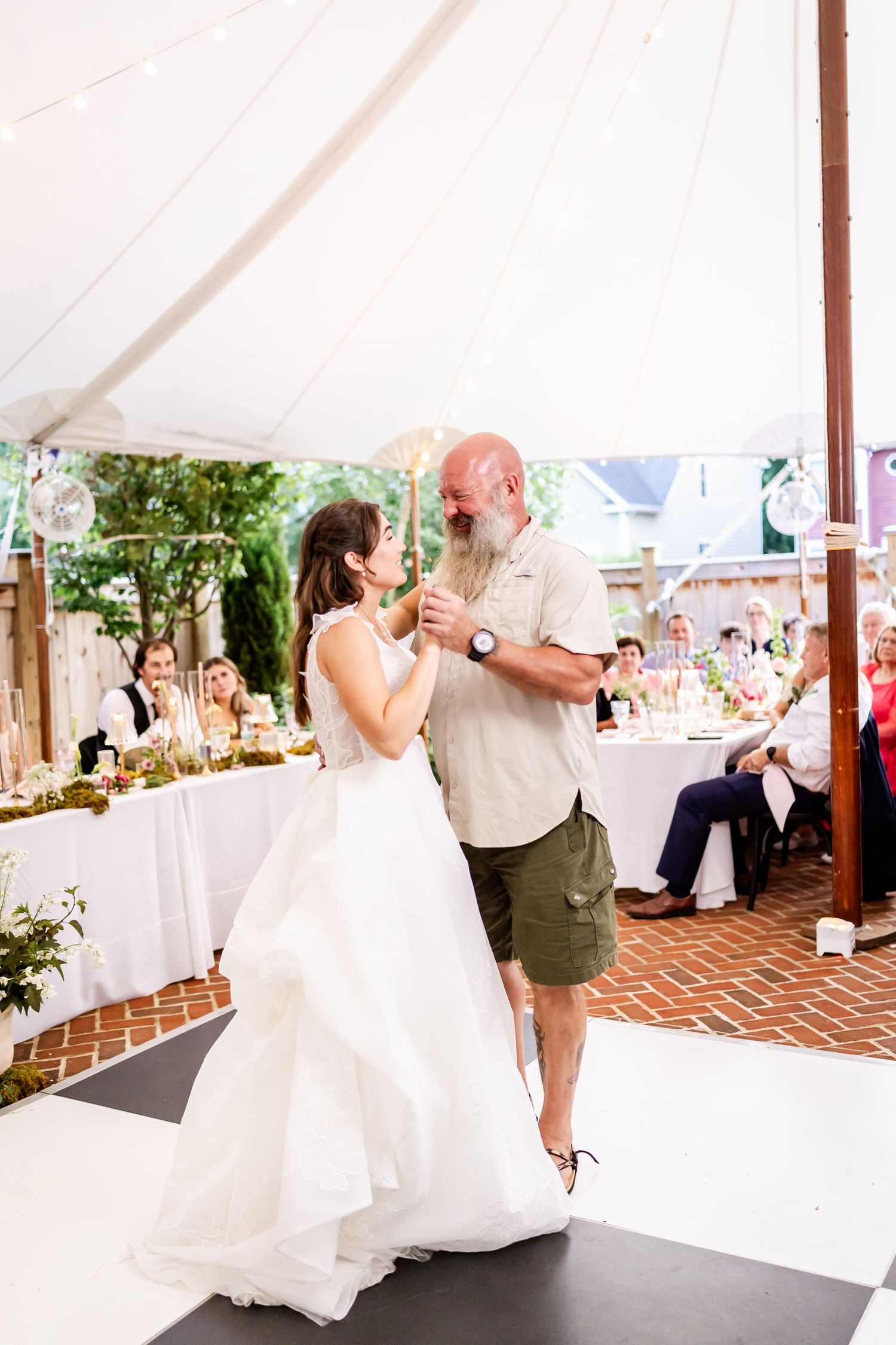 A couple shares their first dance under a white tent at an outdoor wedding reception.