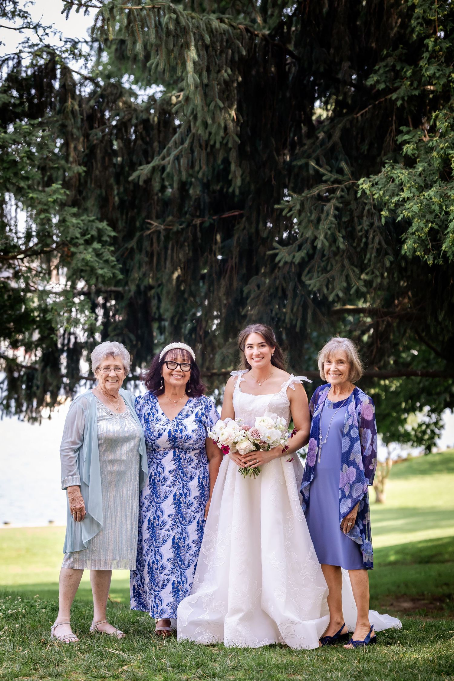 Wedding party poses outdoors under trees wearing blue and white dresses.