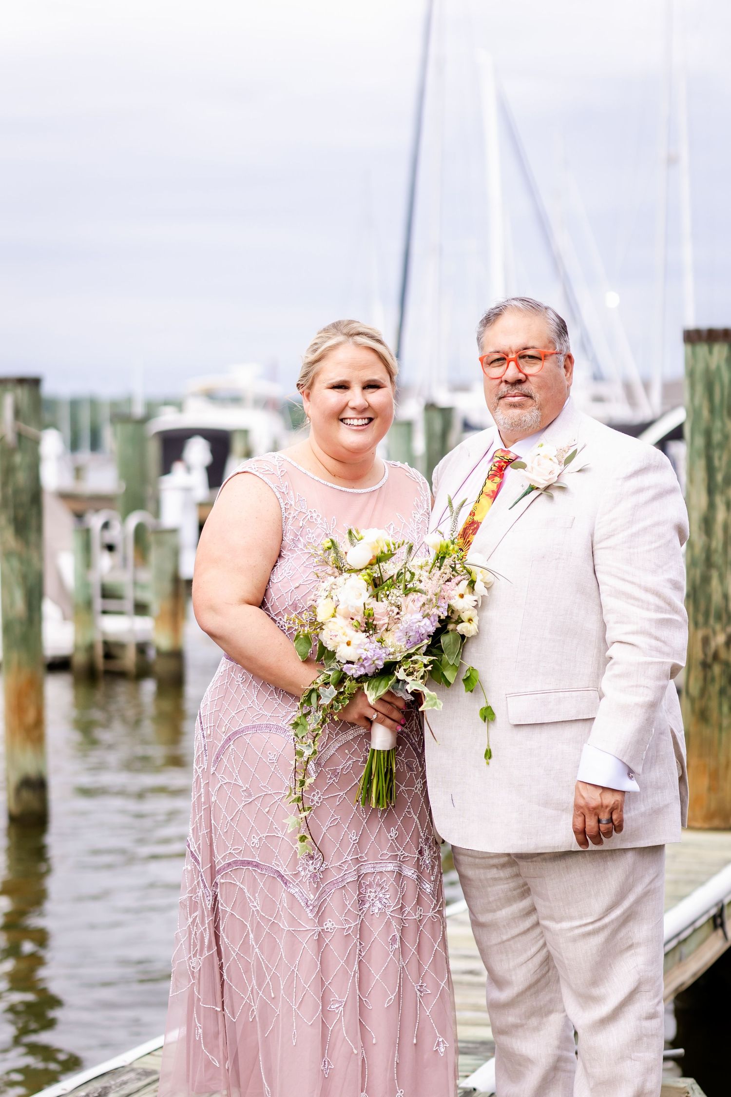 A couple poses on a marina dock in formal attire, with a beautiful floral bouquet against a nautical backdrop.