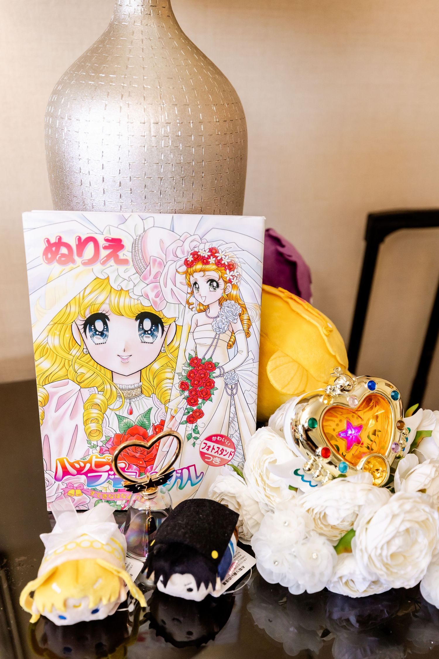 Manga artwork and plush toys arranged with white roses and decorative vase.