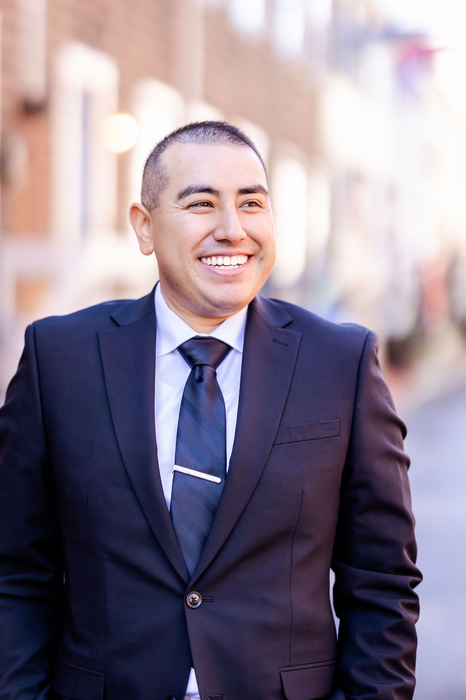 Groom in classic navy suit smiling against urban backdrop.