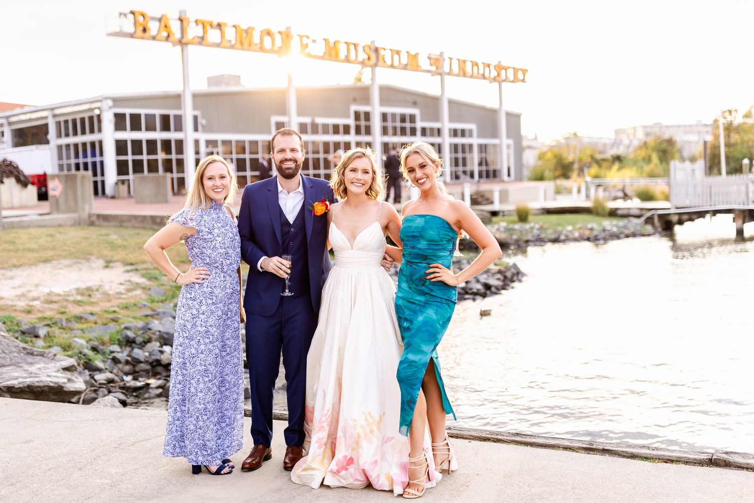 Group photo of wedding party posing in front of Baltimore Trade Center sign near the water.