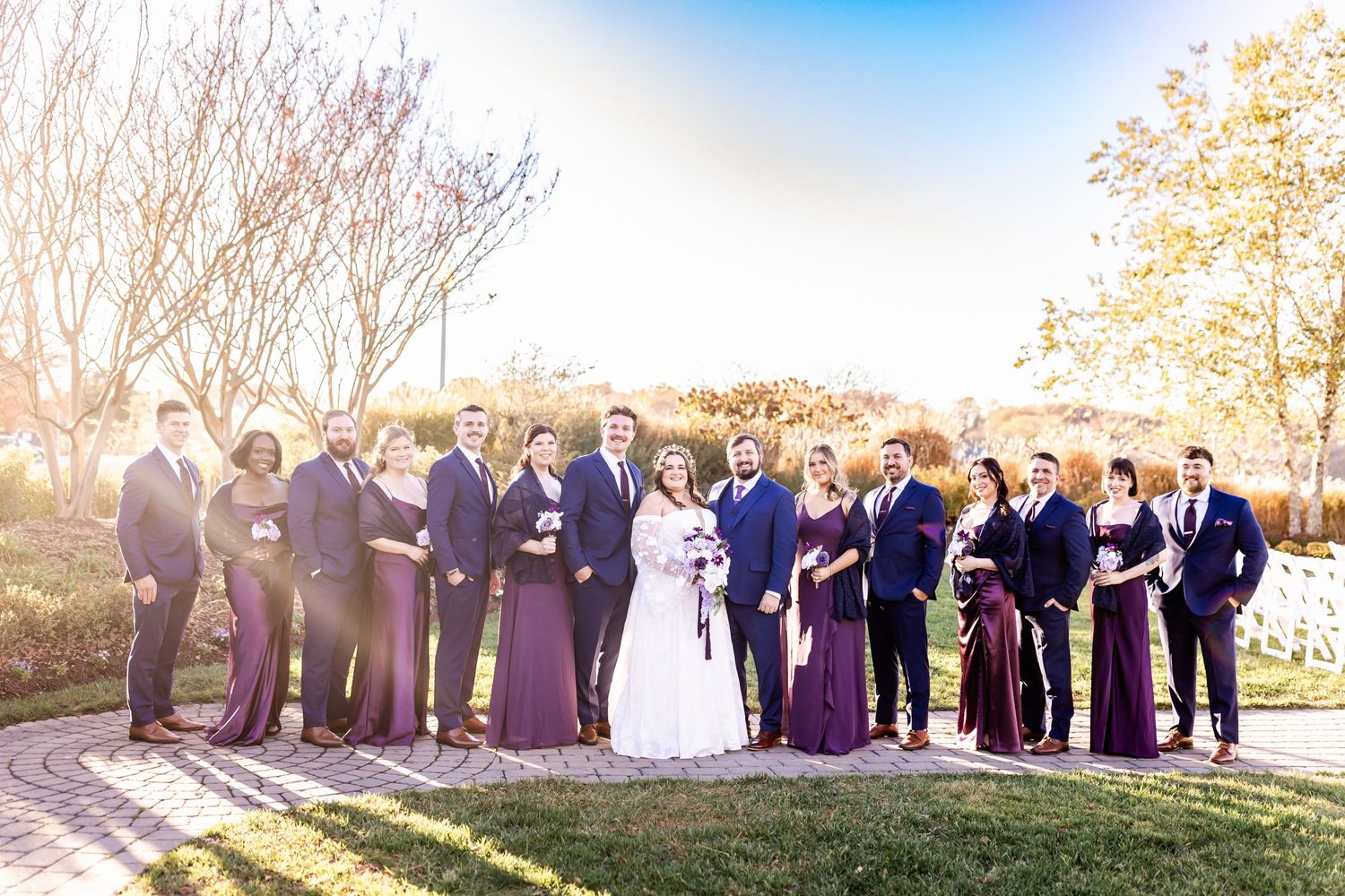 Wedding party lined up on stone pathway wearing coordinated purple and navy formal attire.