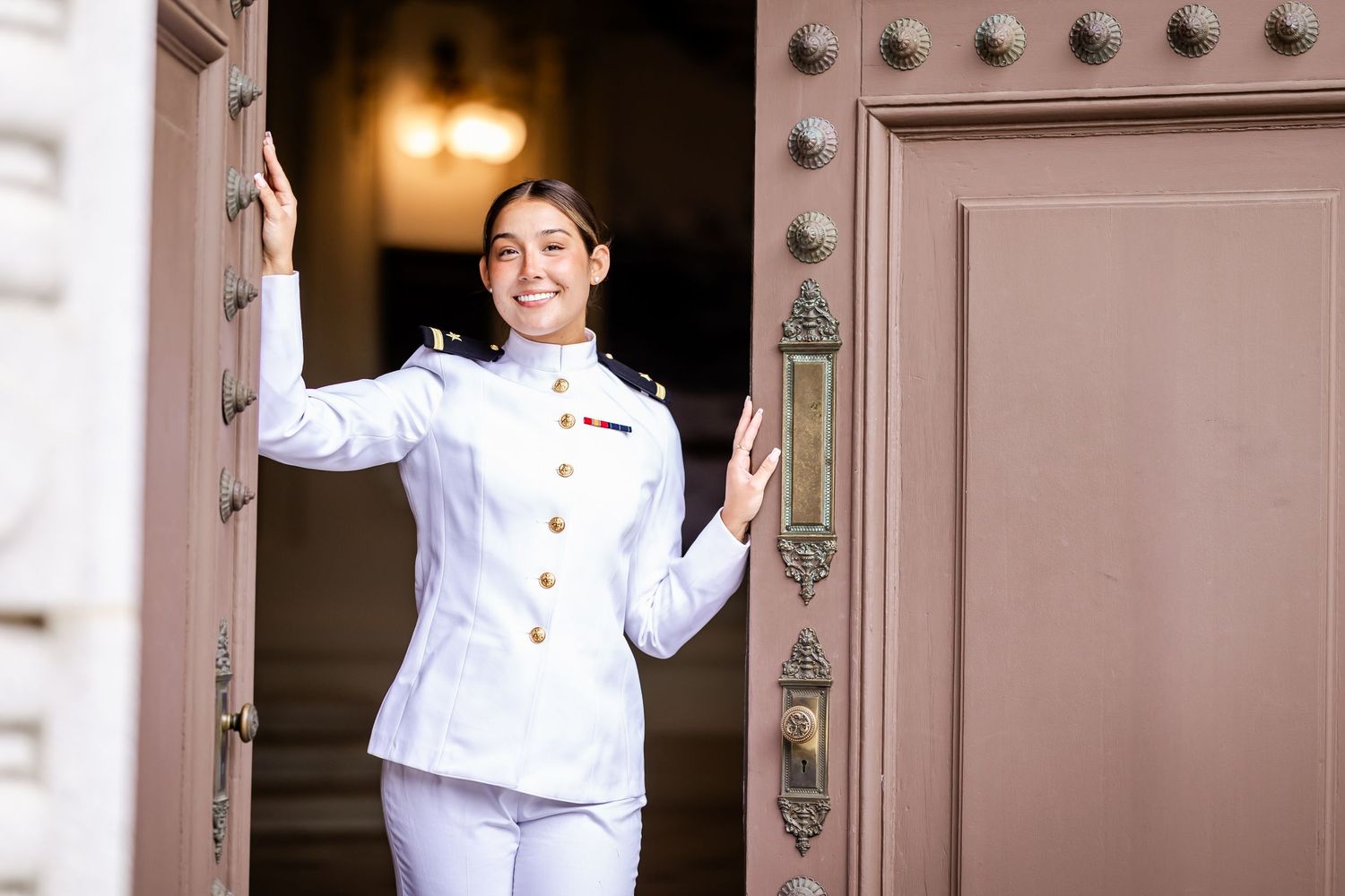 Military personnel in dress whites standing against metal door background.