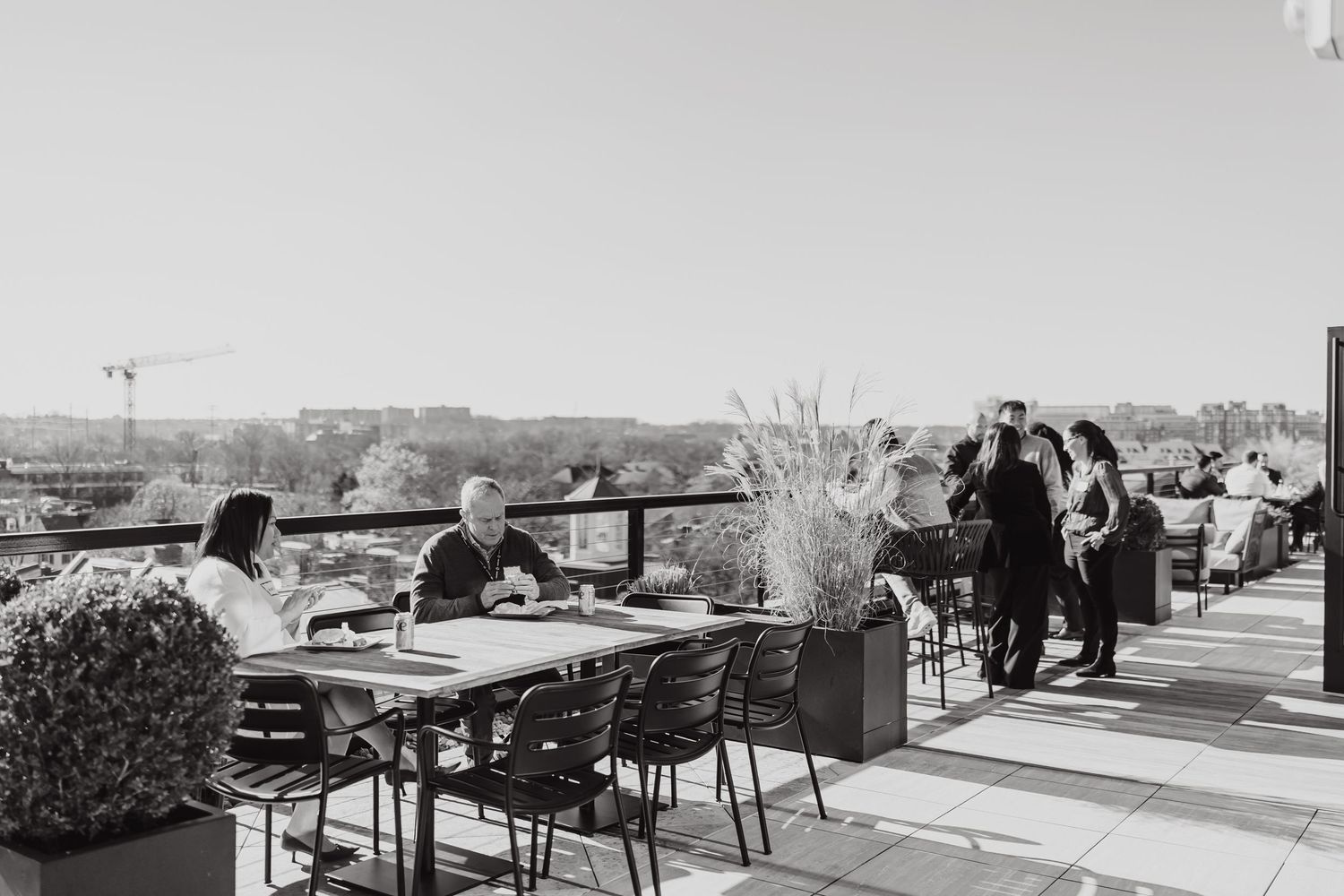 Black and white photo of outdoor rooftop dining area with tables and guests enjoying the view.
