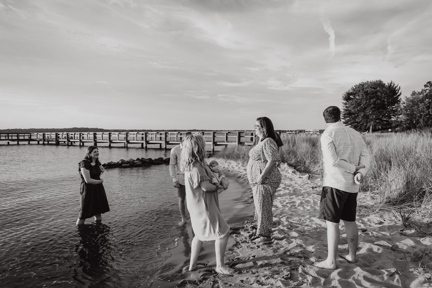 Black and white photo of people gathered on beach near wooden pier.