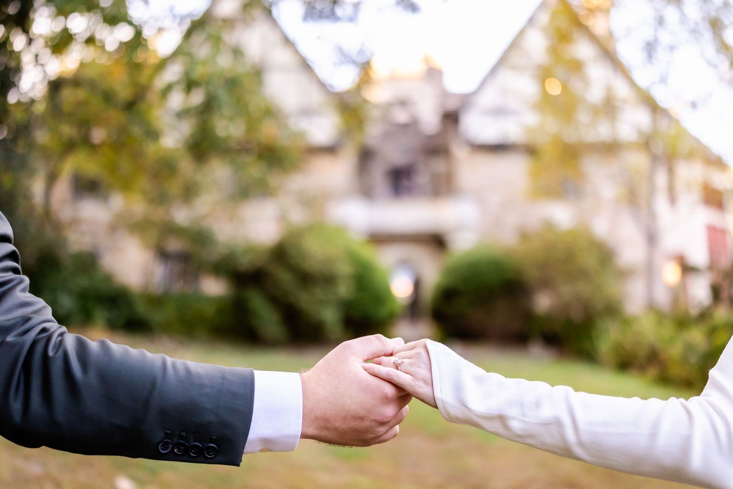 Two hands reaching out to exchange a small object in front of a blurred house exterior on an autumn day.