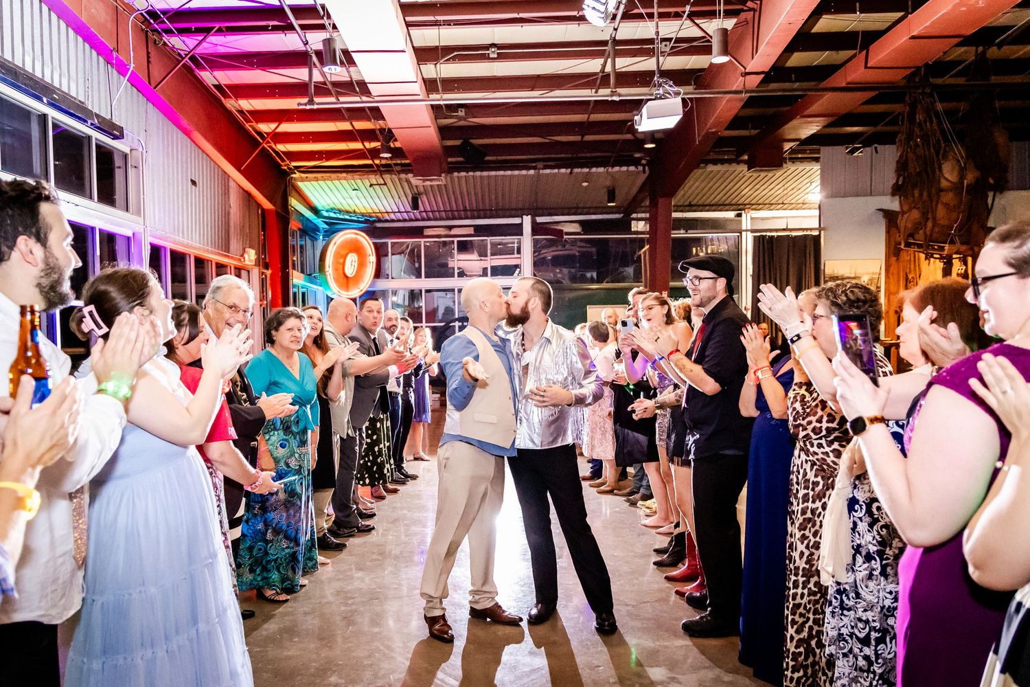 Wedding guests dance and celebrate on a covered outdoor patio decorated with string lights and colorful lighting.