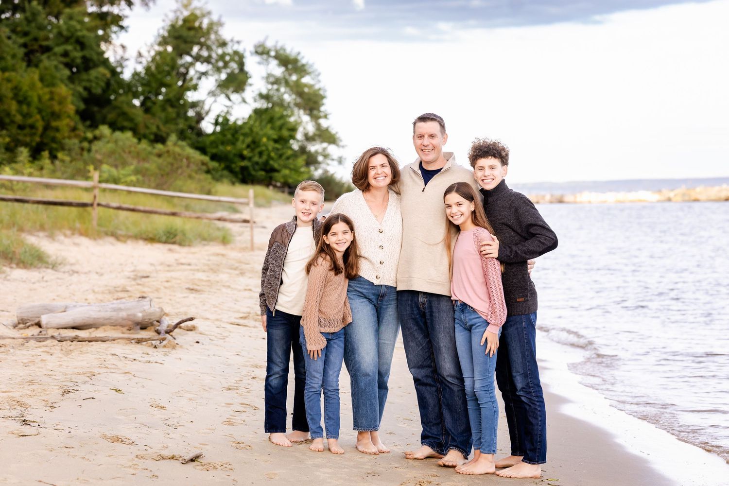 Family group walking and laughing together on a sandy beach during golden hour by the water.