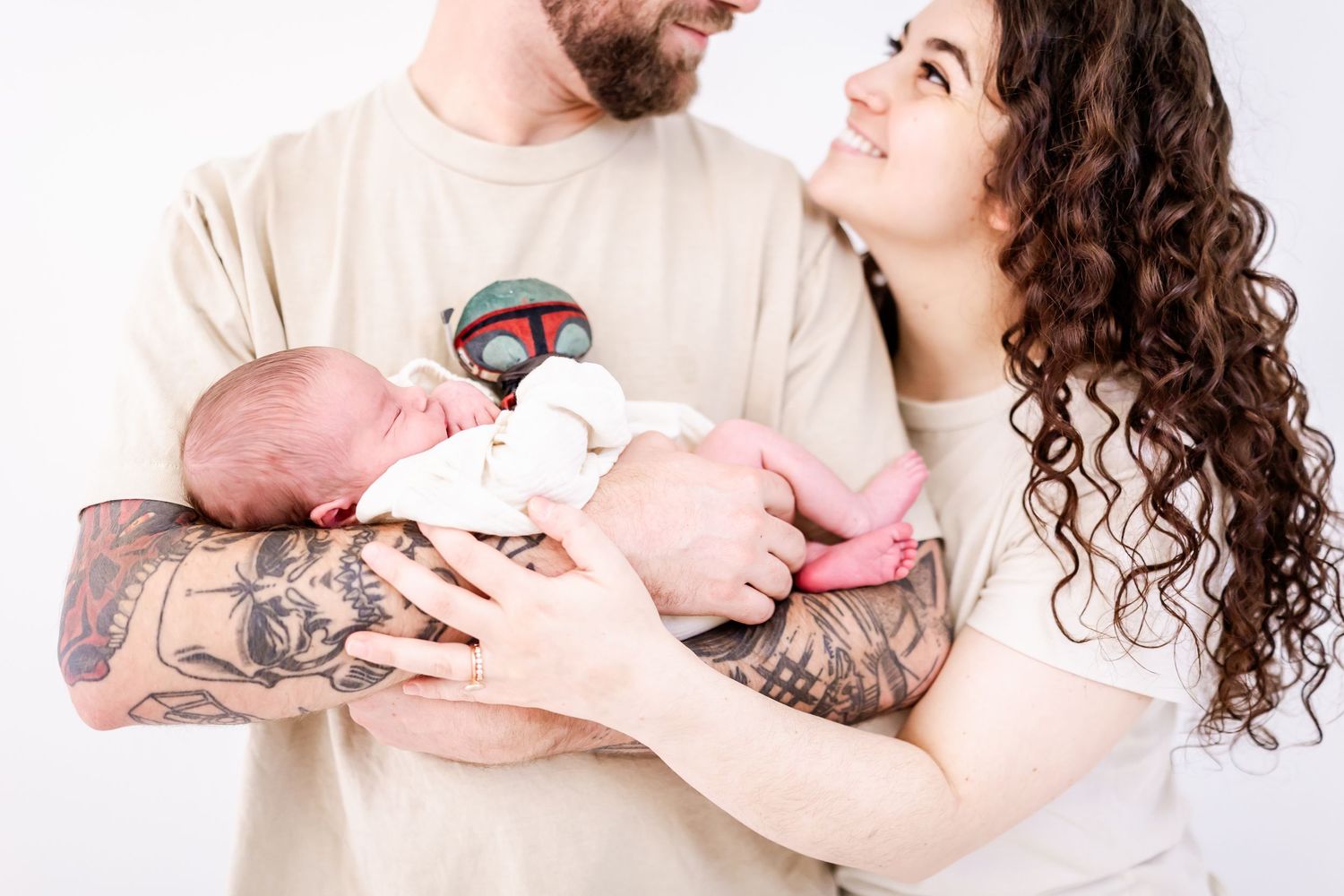 A couple holds their newborn baby together while sharing a tender moment against a white background.