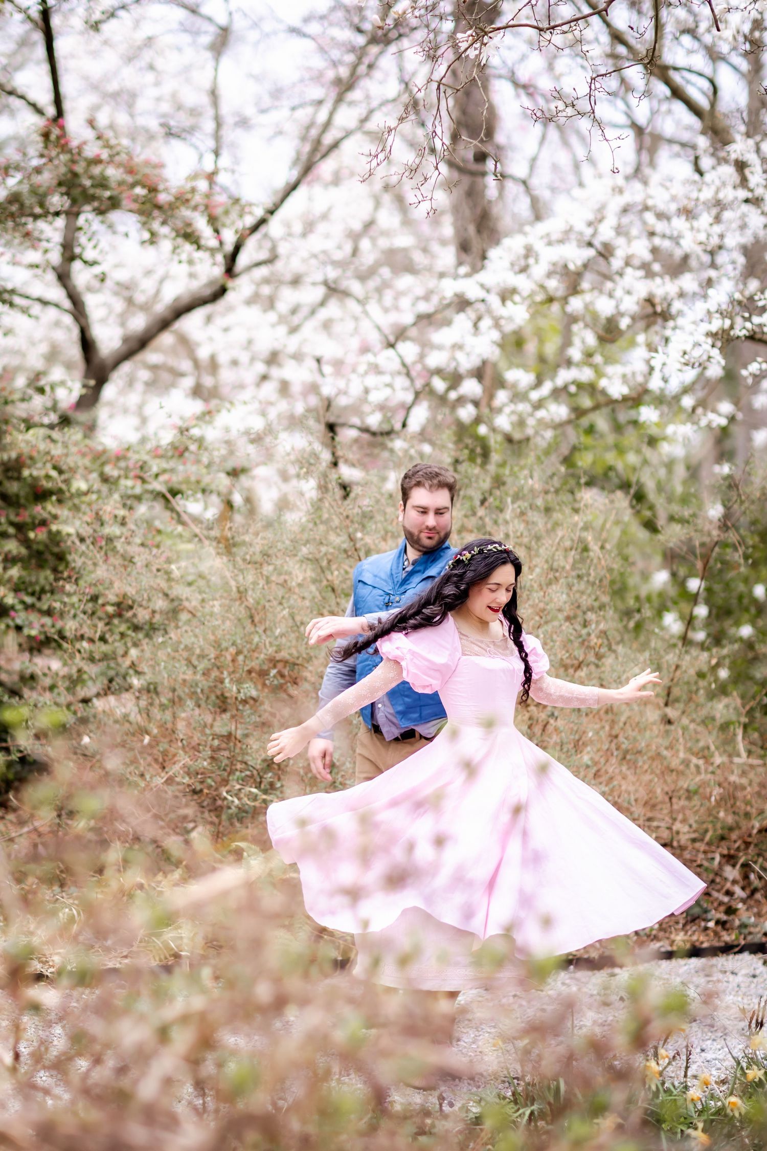 A couple dances playfully among blooming cherry blossom trees in a spring garden setting.