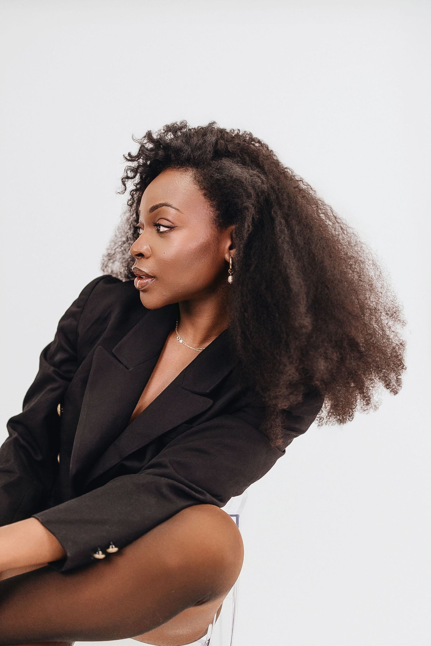A series of four artistic fashion portraits showing a model with voluminous natural curly hair in a black blazer.