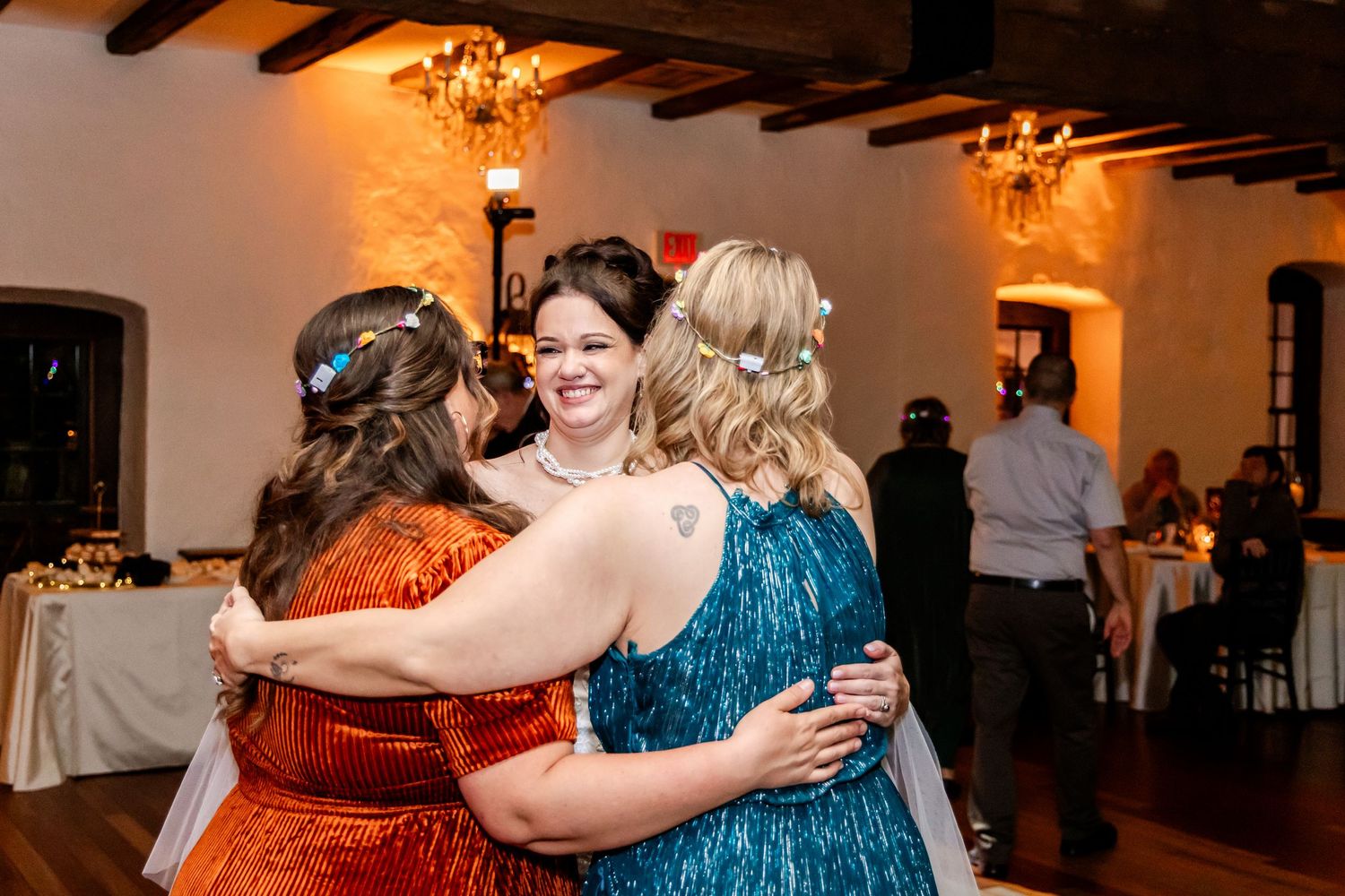Three wedding guests share a joyful group hug on the dance floor during the reception.