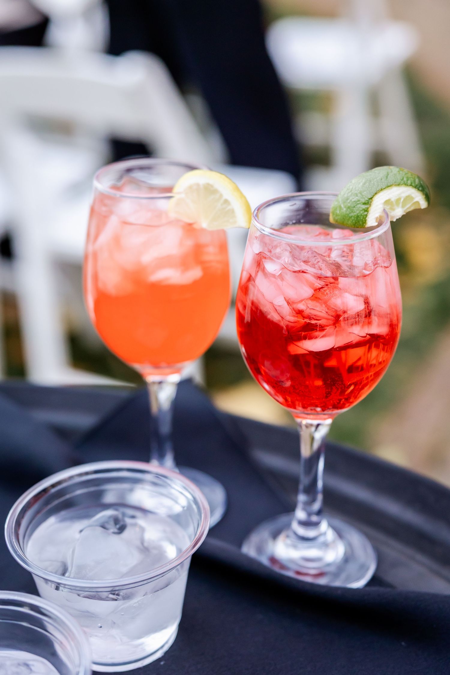 Colorful pink and red cocktails garnished with citrus and ice in elegant stemmed glasses on a dark surface.