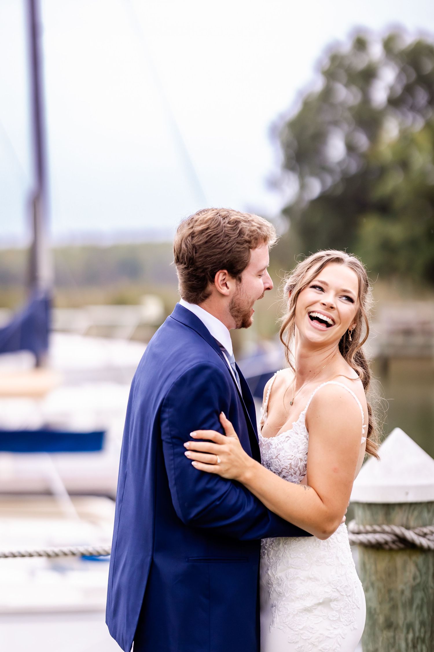 Newlyweds sharing joyful laughter on a dock with boats in the background.