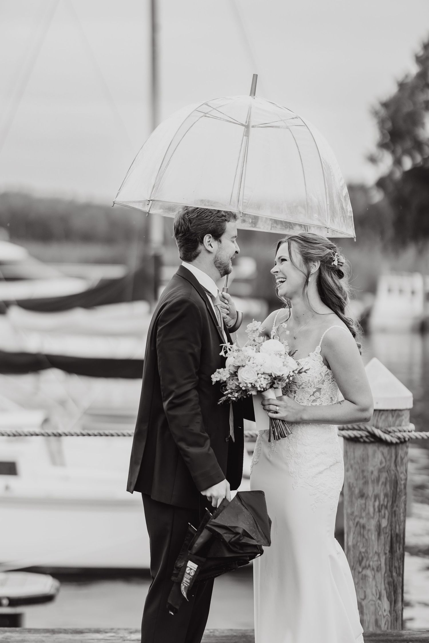 Black and white photo of couple sharing intimate moment under clear umbrella during wedding.