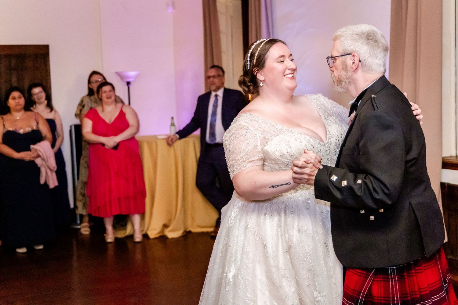 Wedding couple in formal attire dancing at a reception with guests watching in the background.