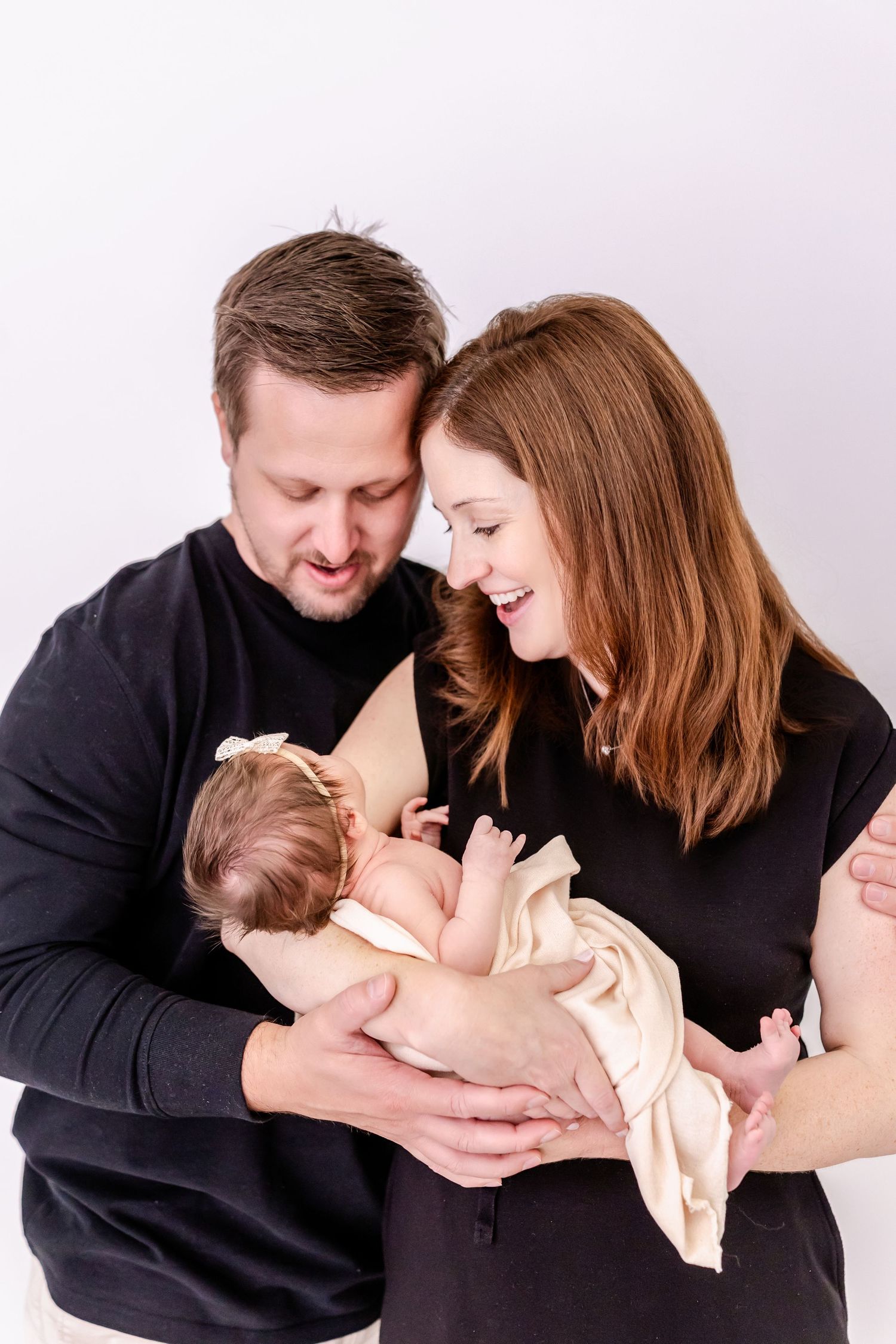 Family shares tender moments with their newborn baby in a series of intimate studio portraits on white background.
