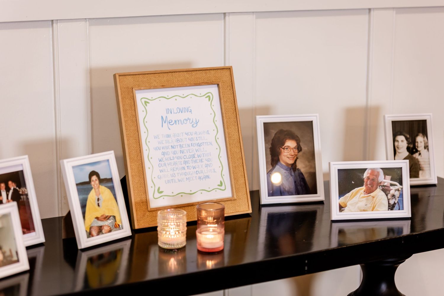 Row of framed photographs and certificates displayed on a white wall with candle holders.
