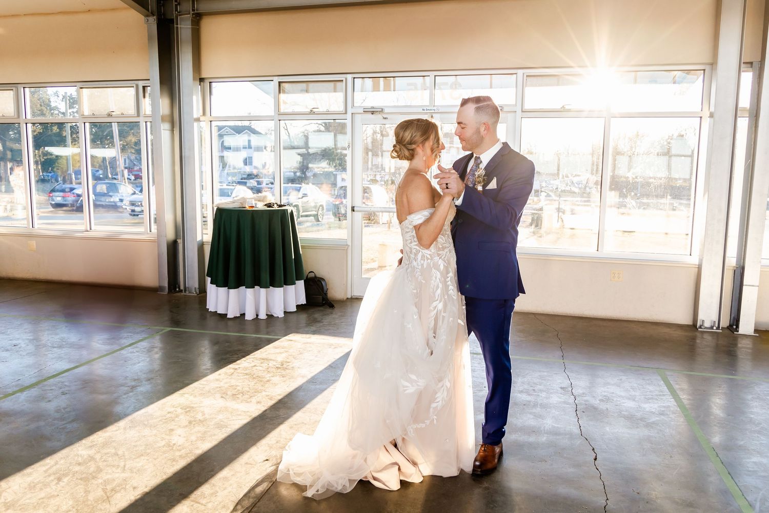 A couple shares their first dance in a sunlit wedding venue.