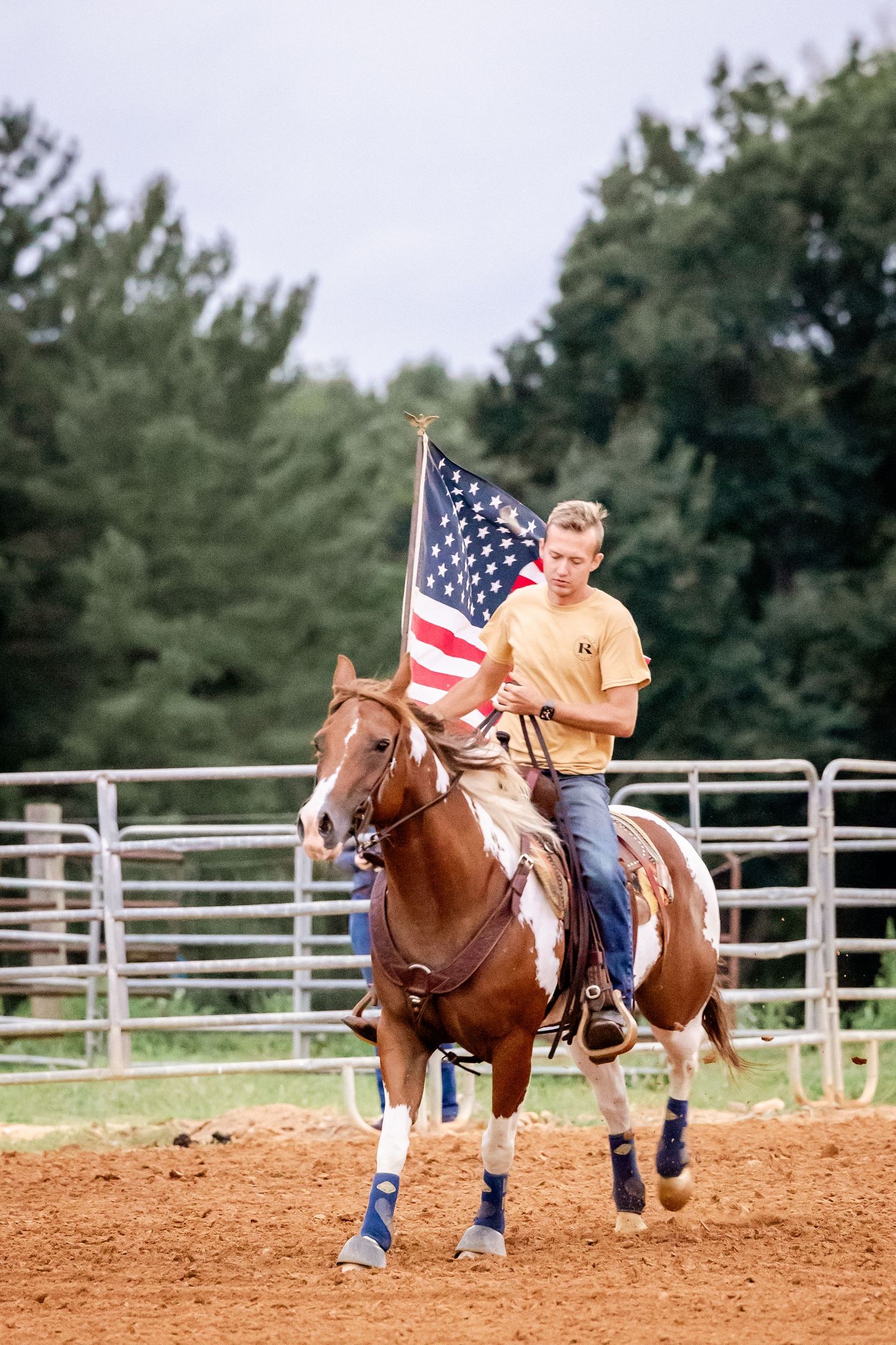 Rider carries American flag while riding horseback in western arena.