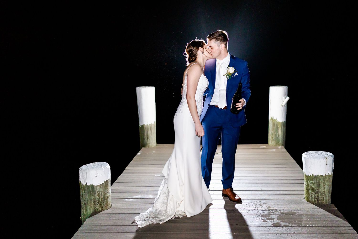 Newlyweds embrace on moonlit pier during evening wedding celebration.