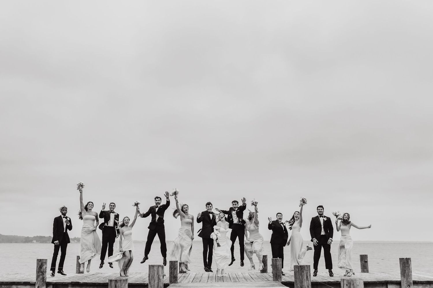 Wedding party silhouettes strike fun poses against an overcast sky for a creative group photo.
