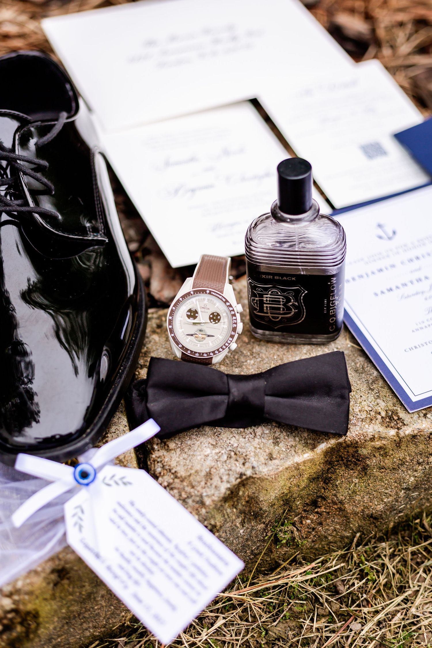 Wedding accessories including bow tie, perfume bottles, and invitation cards on textured surface.