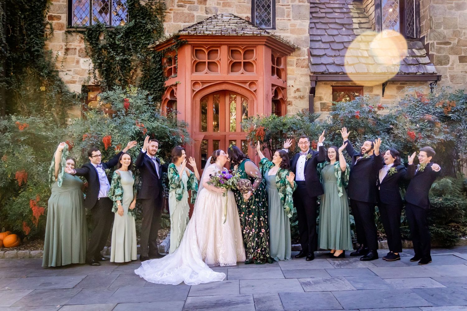 Large wedding party poses on stone steps in front of historic building with sage green accents.