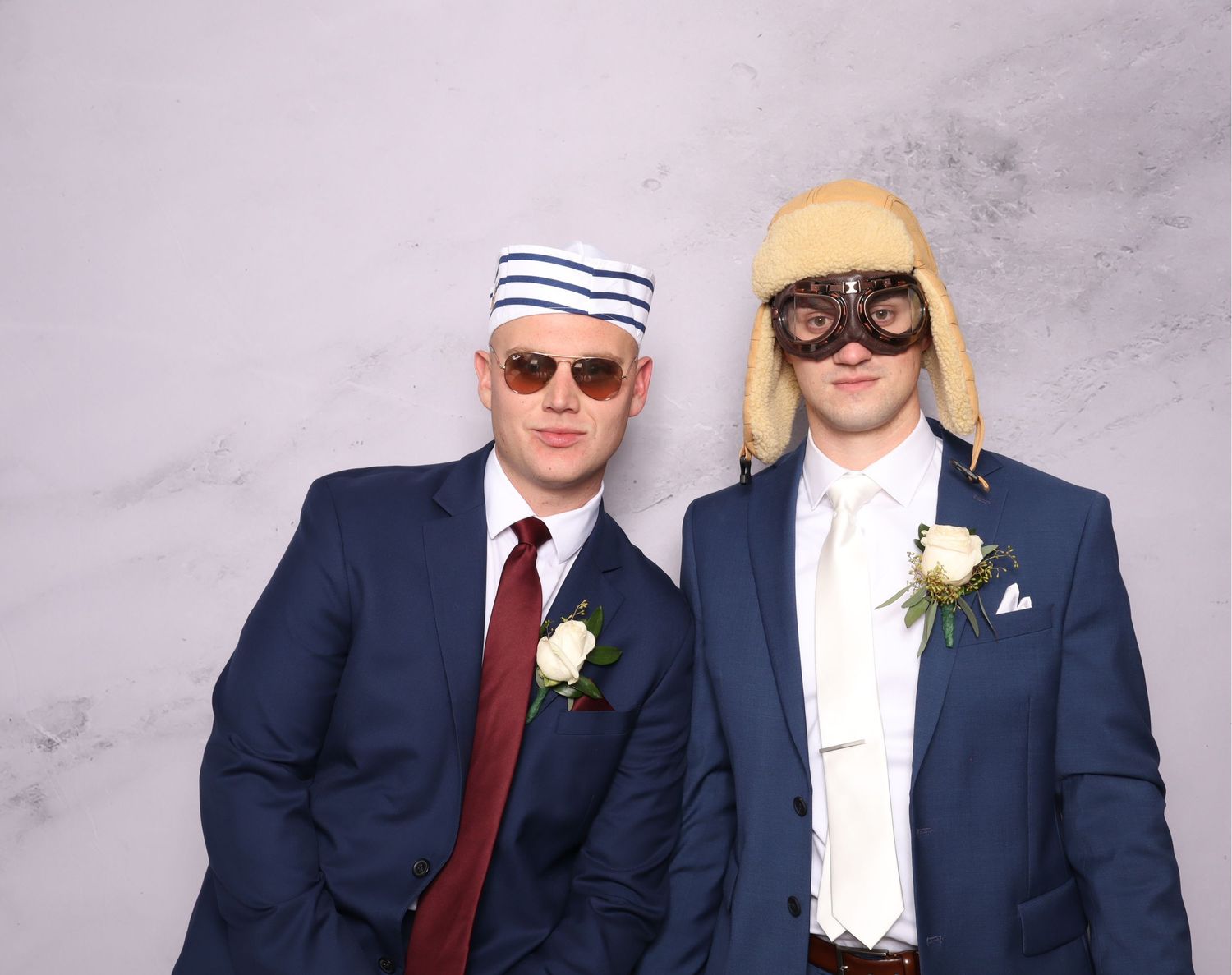 Wedding party members in navy suits and burgundy ties pose together against a gray backdrop.