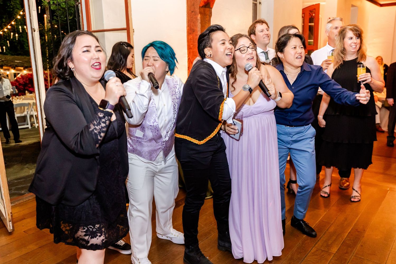 Group of party guests singing and dancing enthusiastically at an indoor celebration venue.