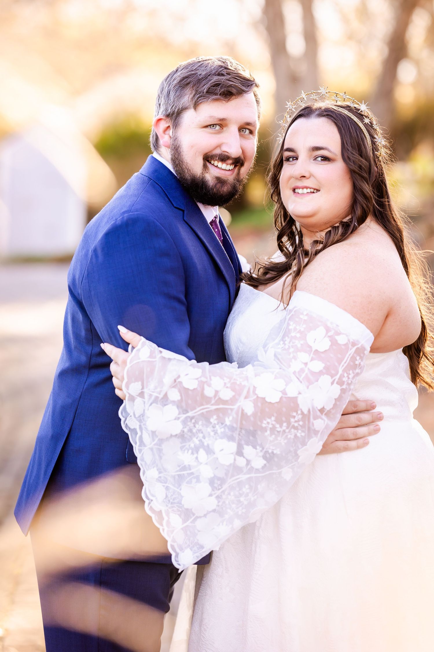 A wedding couple embraces while showcasing the bride's detailed lace dress.