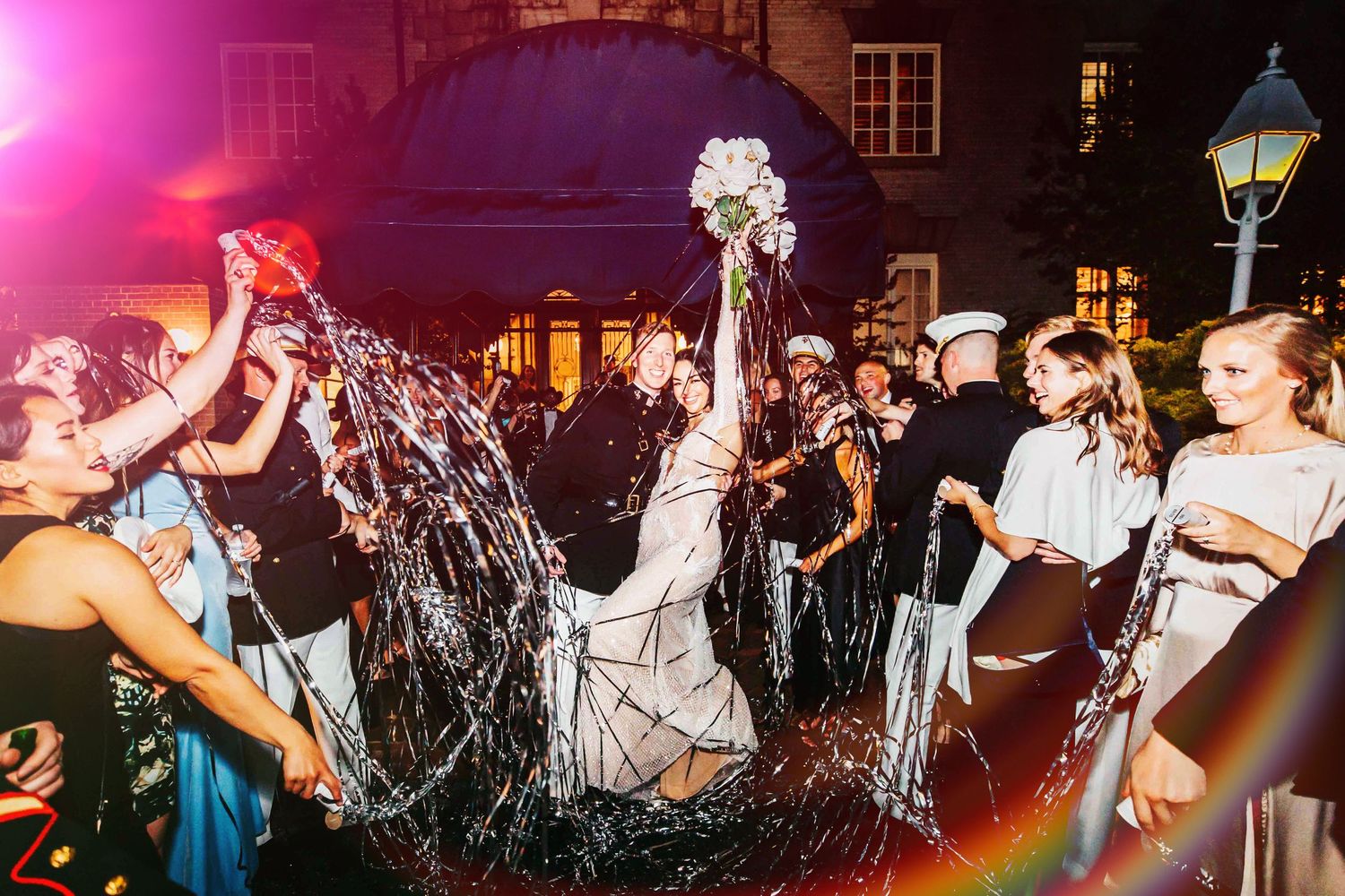 A joyful celebration outdoors at night with sparklers and laughter among festively dressed people at an evening event.