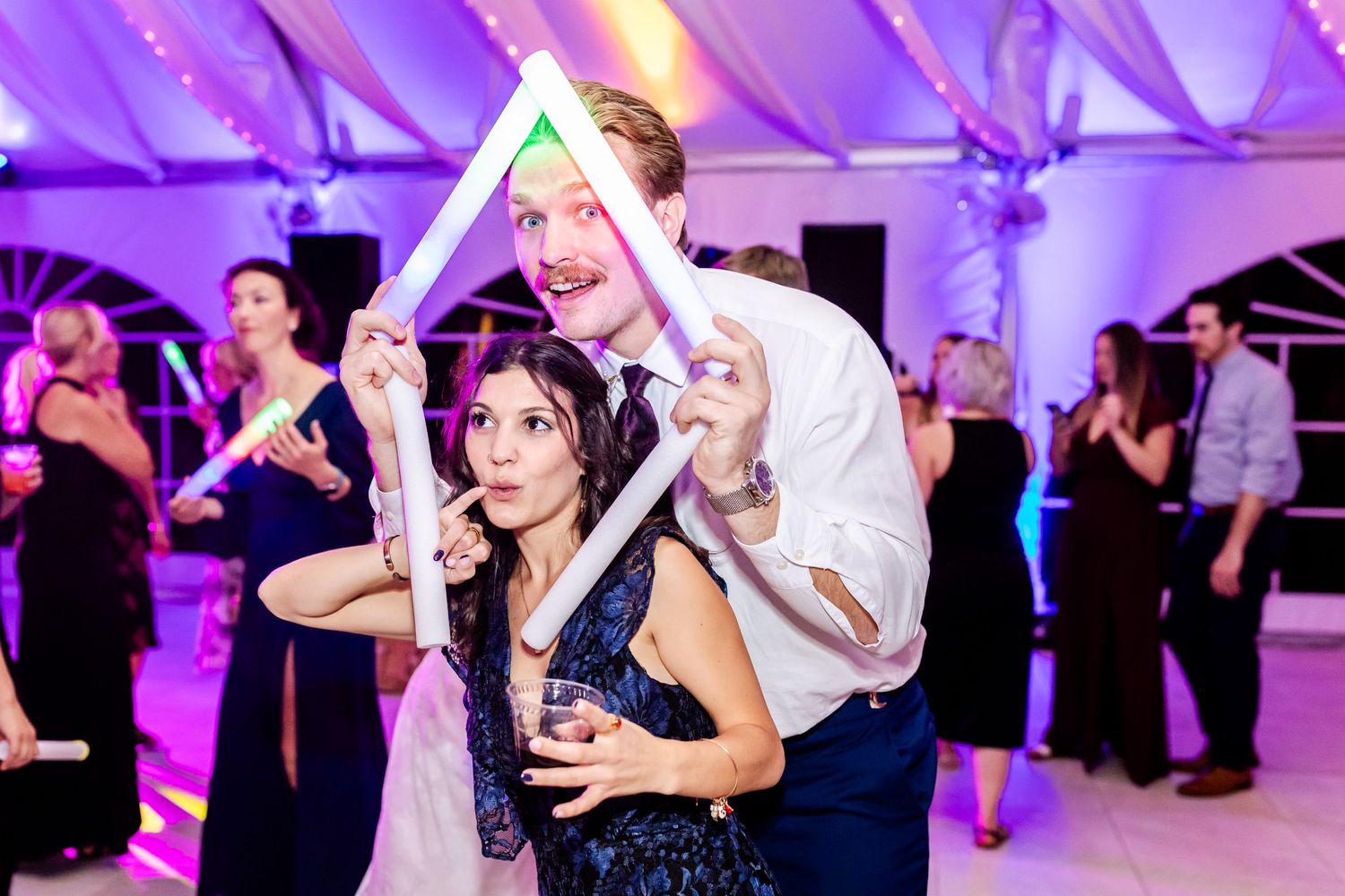 Dancing couples enjoying festive moment under purple-lit tent at wedding reception.