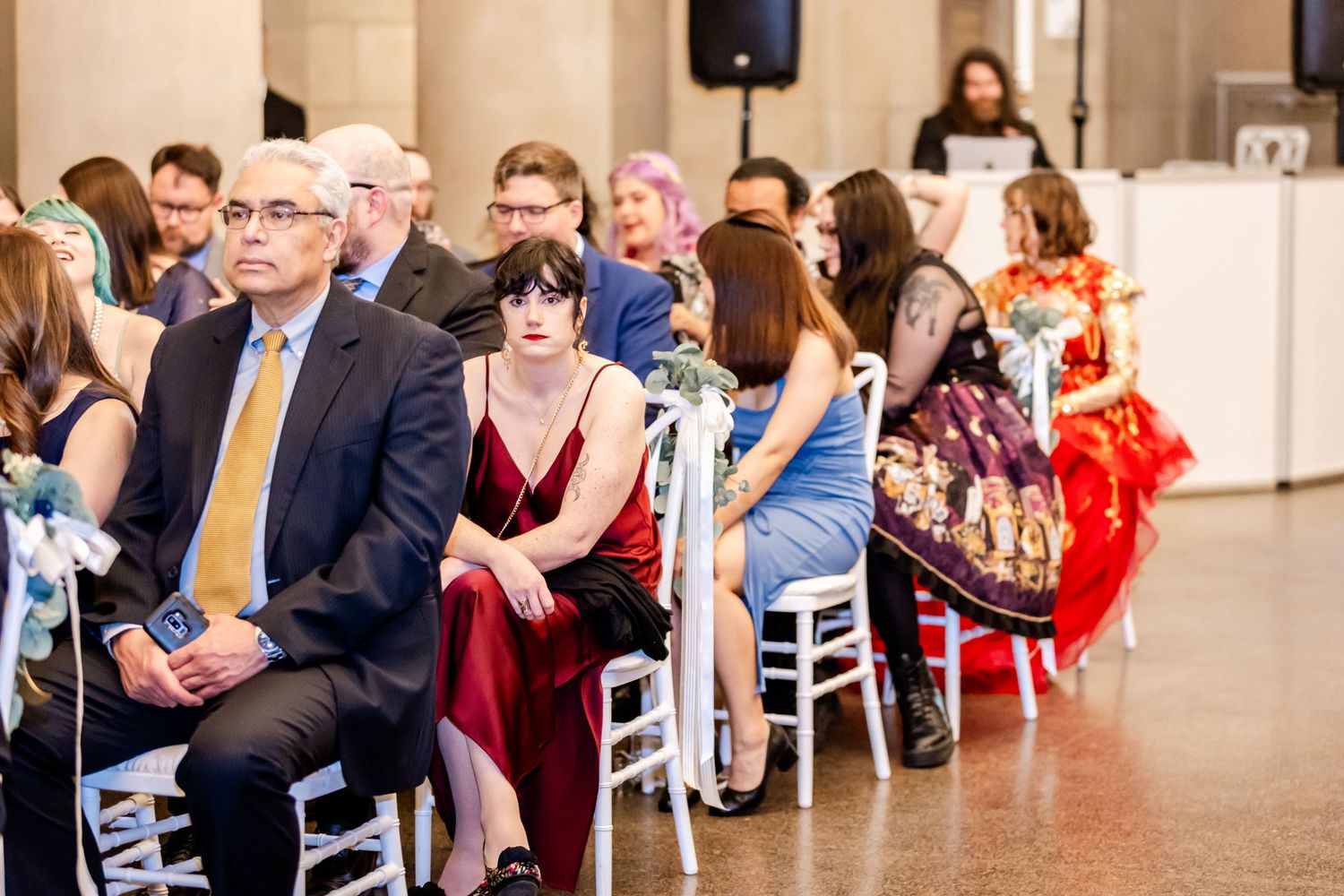 Wedding ceremony guests seated in white chairs with decorative red accents in an elegant venue.