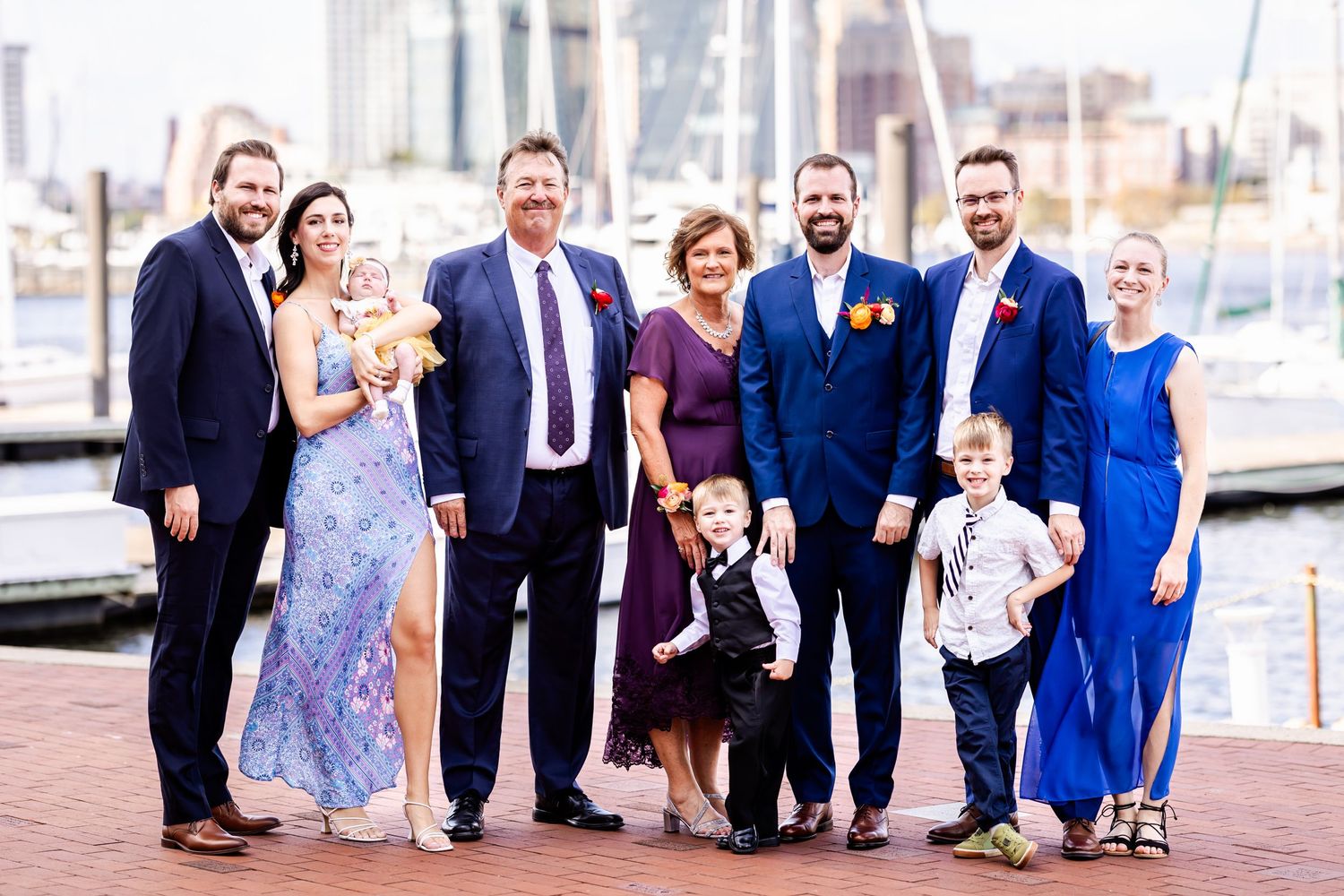 A wedding party poses together on a waterfront boardwalk in formal attire.